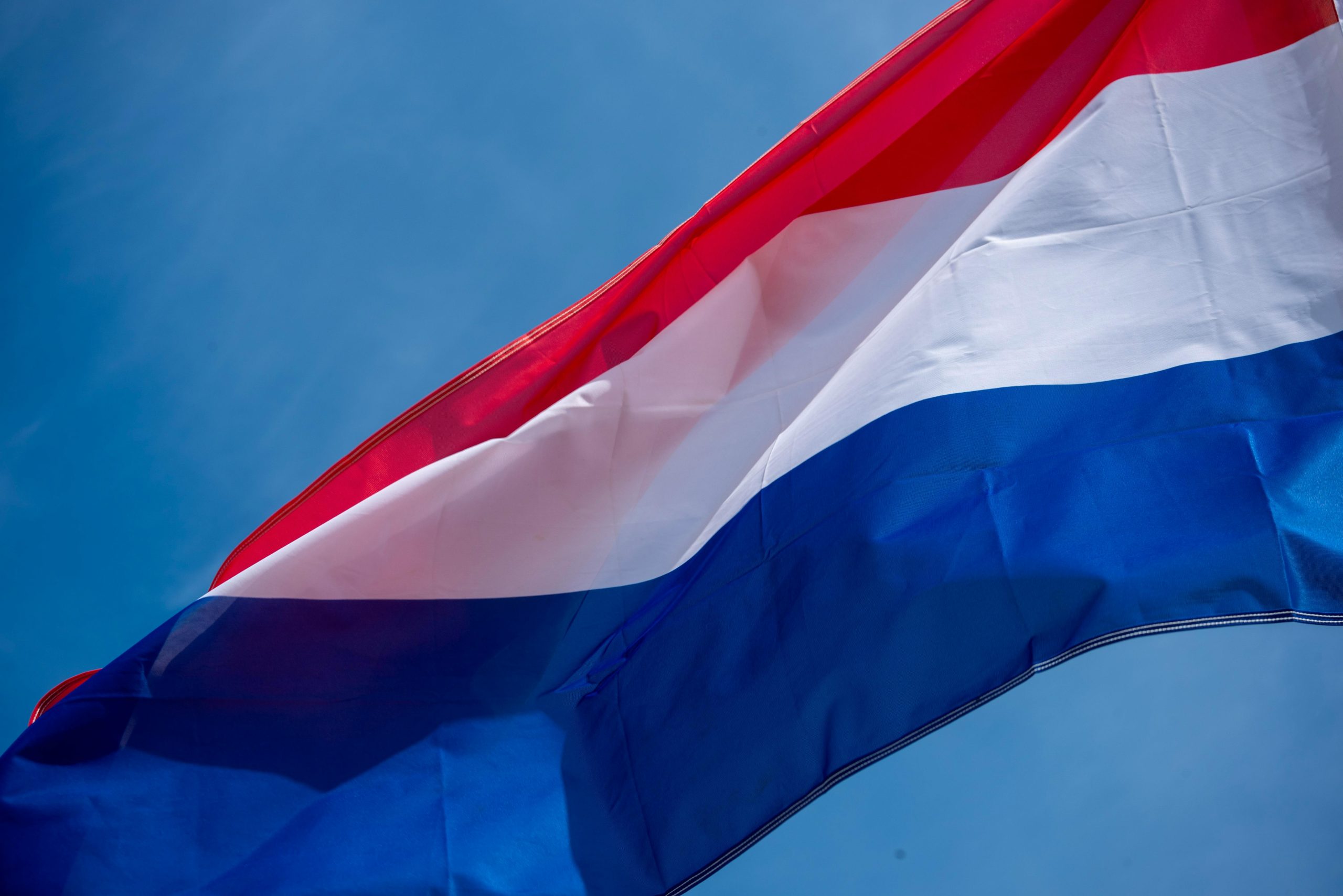 A dynamic shot of the Netherlands flag waving against a clear blue sky, symbolizing freedom and patriotism.
