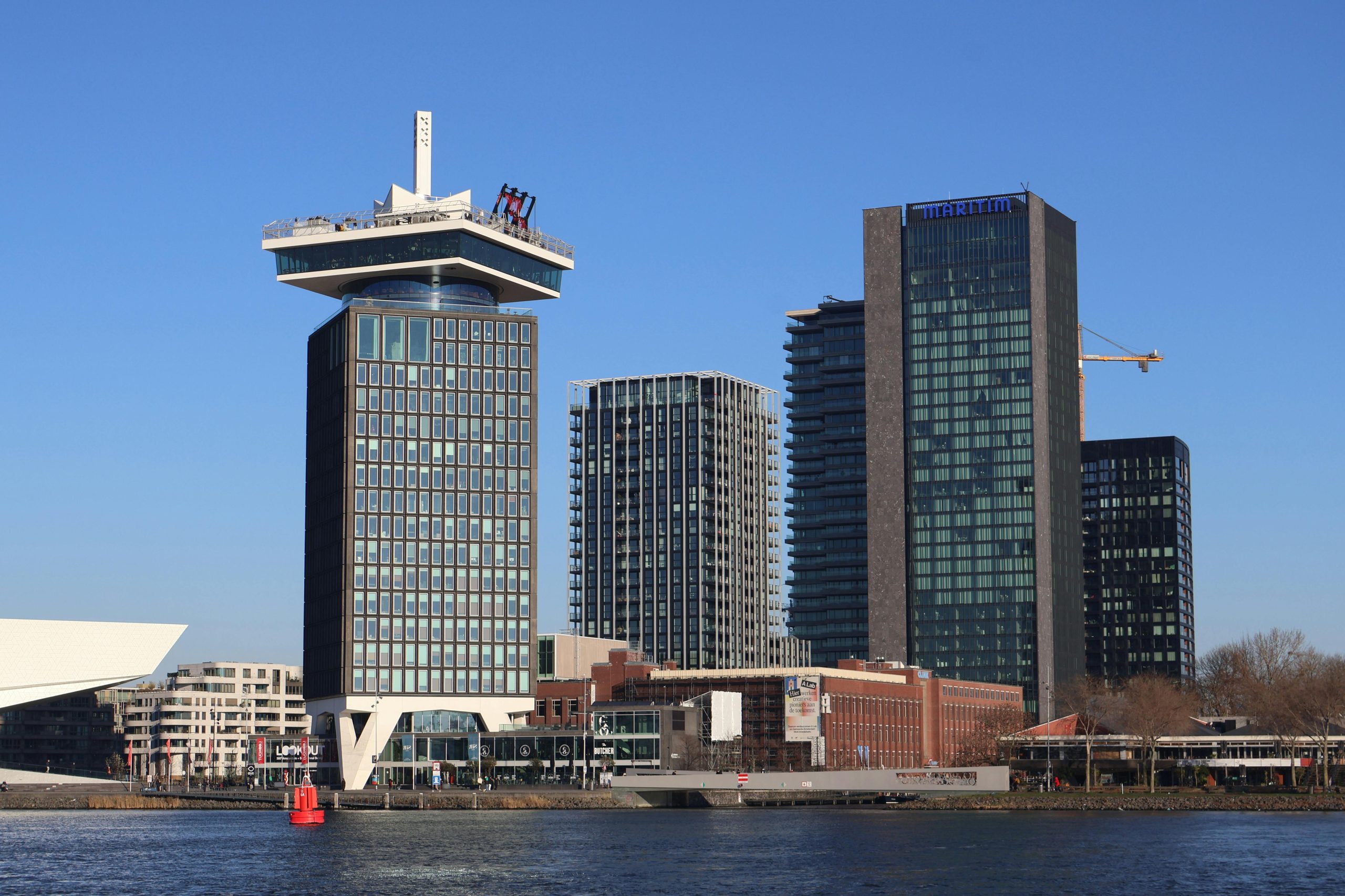 Skyscrapers overlooking the river in Amsterdam, showcasing modern architectural designs under a clear blue sky.