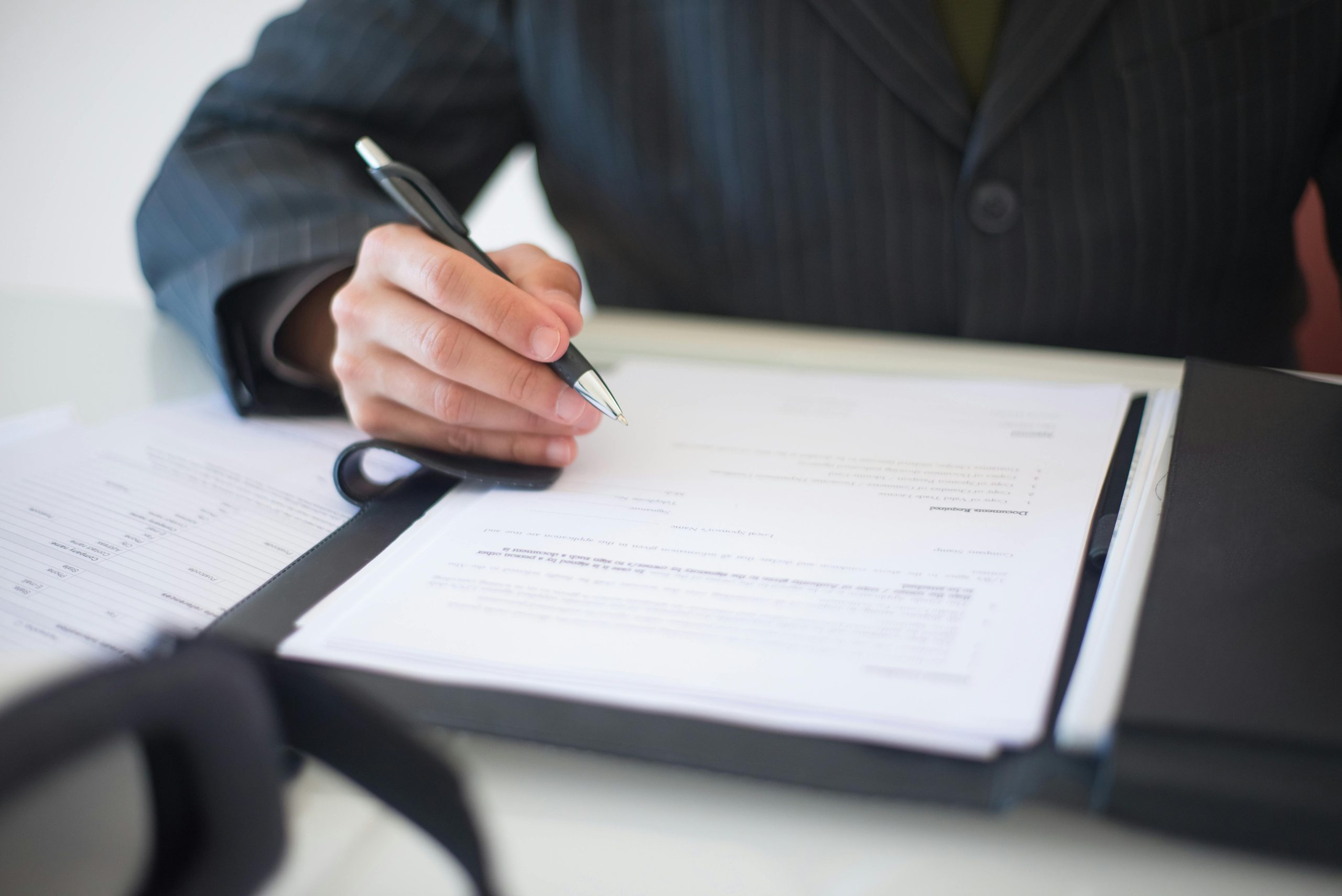Home Close-up of a hand signing documents with a pen, symbolizing an important business contract.
